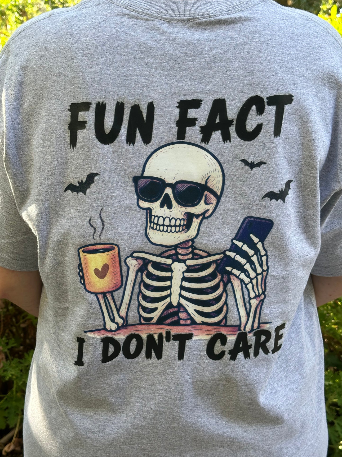 Gray t-shirt with a skeleton graphic and text 'Fun Fact I Don't Care' on a grassy background
