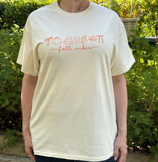 Person wearing a white t-shirt with 'Pumpkin spice fall vibes' text in an outdoor setting