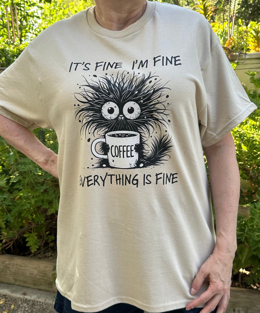Beige t-shirt with a graphic and text 'It's fine, I'm fine, everything is fine' and a coffee cup.