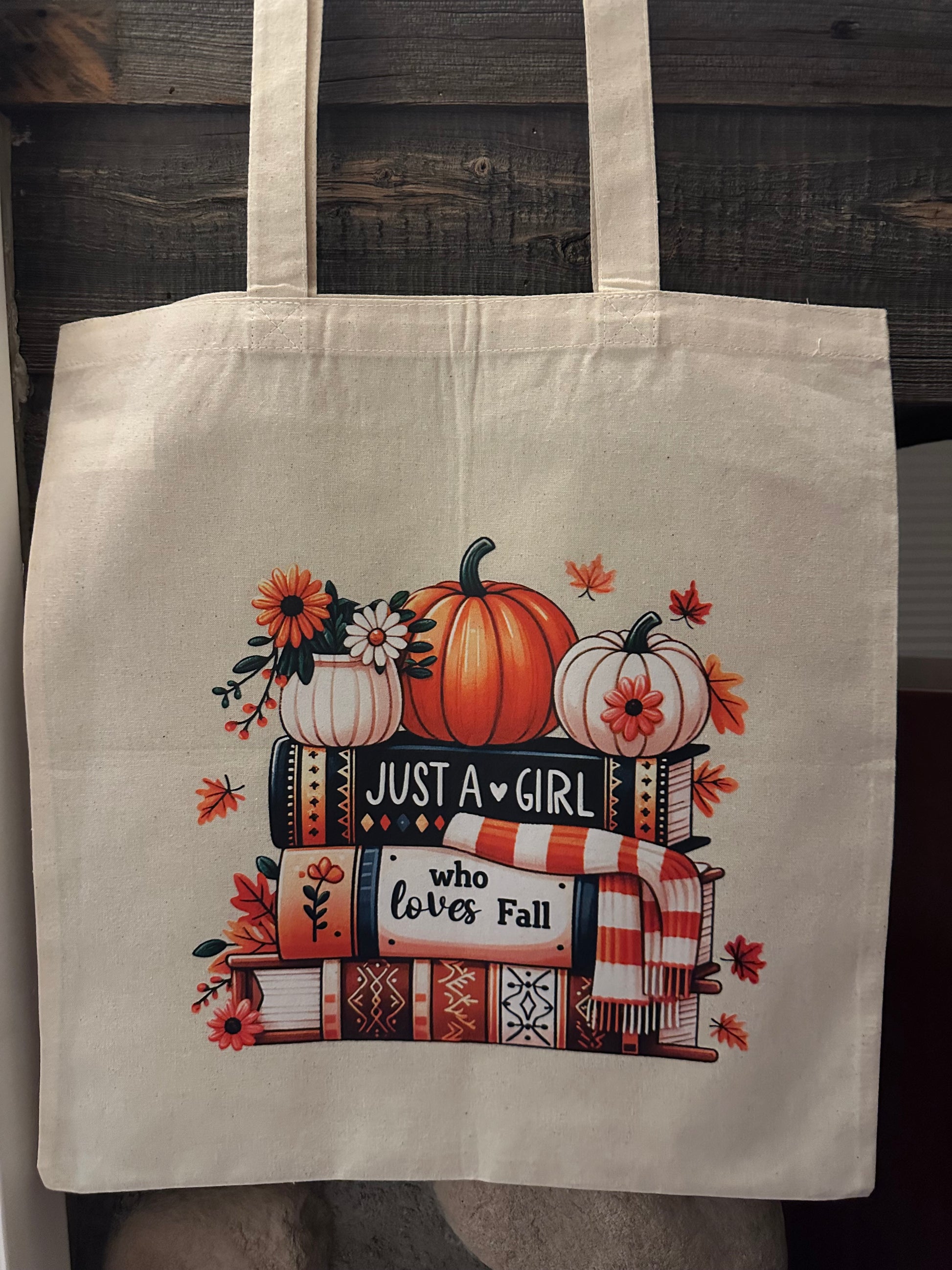 Tote bag with autumn-themed design featuring pumpkins and books on a wooden surface.