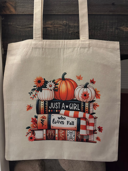 Tote bag with autumn-themed design featuring pumpkins and books on a wooden surface.