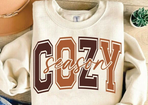 Folded sweatshirt with 'COZY season' text on a wooden surface